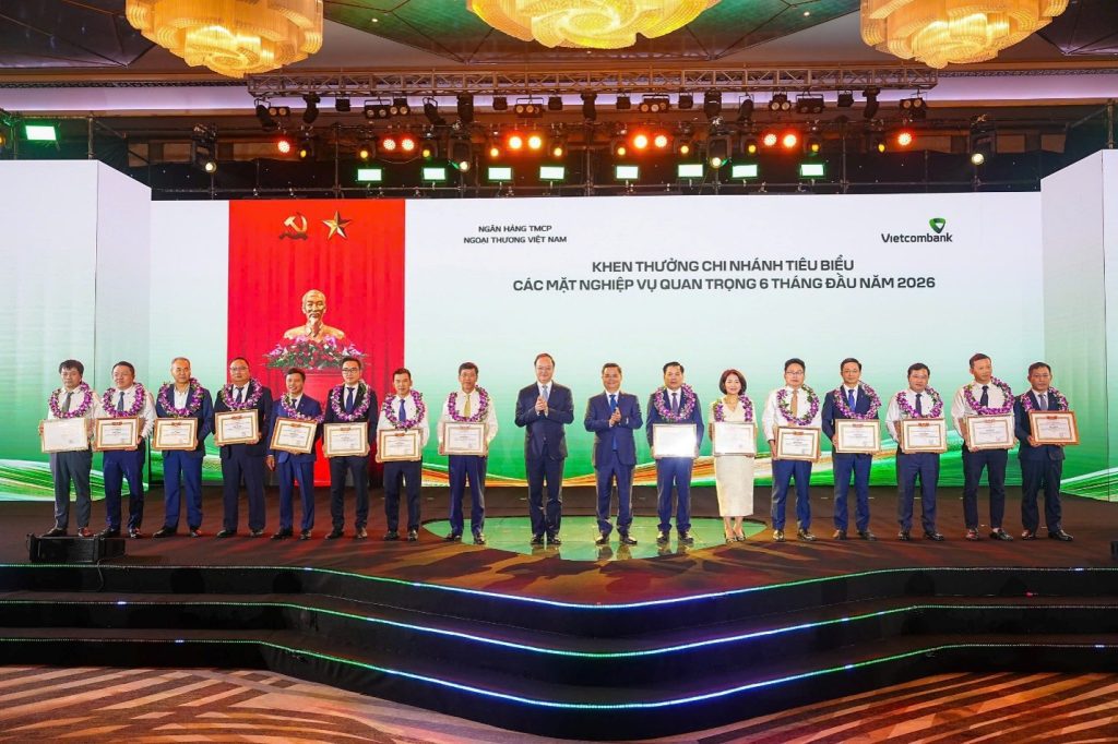 : Đ/c Nguyễn Thanh Tùng - Bí thư Đảng ủy, Chủ tịch HĐQT Vietcombank (thứ 8 từ phải sang) tặng giấy khen và đ/c Lê Quang Vinh - Phó Bí thư Đảng ủy, Thành viên HĐQT, Tổng Giám đốc Vietcombank (thứ 9 từ phải sang) trao hoa chúc mừng cho 15 chi nhánh tiêu biểu trong hoạt động kinh doanh 6 tháng đầu năm 2026